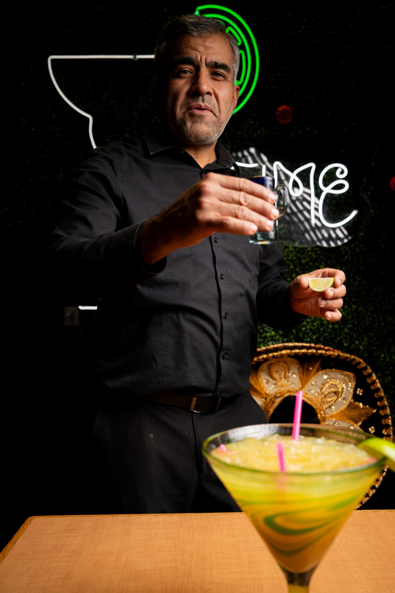 Bartender pouring a shot beside a frozen margarita